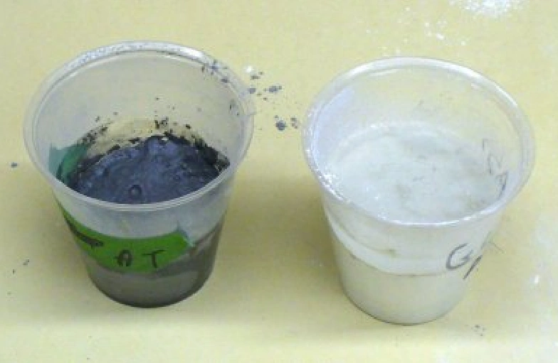 Two plastic cups, one containing a dark muddy liquid and the other filled with cloudy white water, placed side by side on a yellow surface.