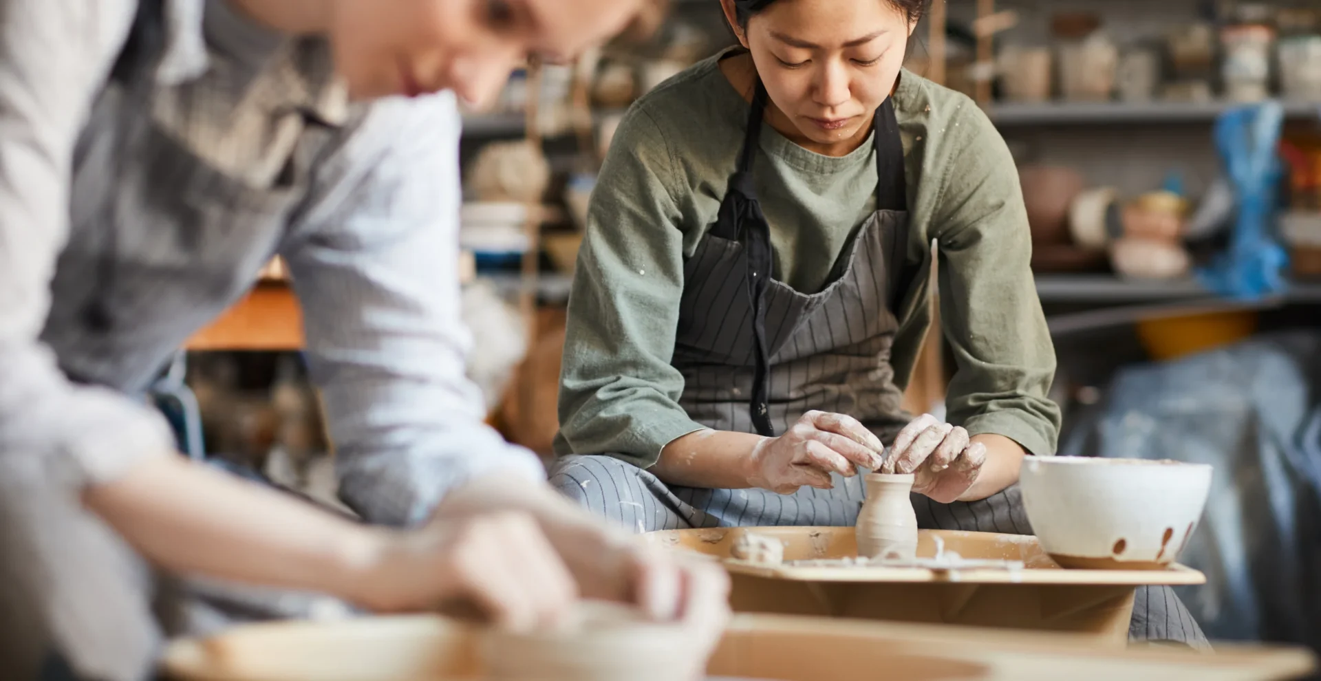 Two women focused on shaping clay pottery by hand in a ceramics studio.