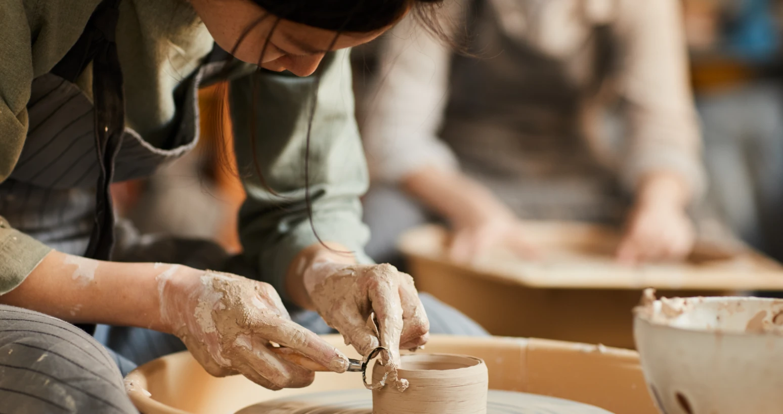 Close-up of a person shaping clay on a pottery wheel while wearing an apron in a pottery studio.