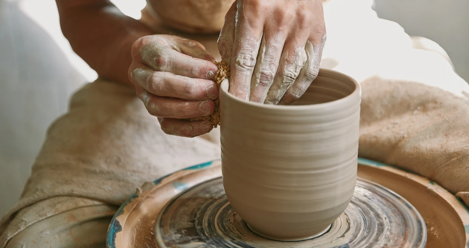 Hands shaping a clay pot on a pottery wheel, demonstrating the ceramic crafting process.