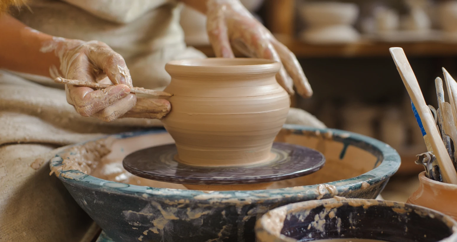 Close-up of hands shaping a clay pot on a pottery wheel in a ceramic workshop.